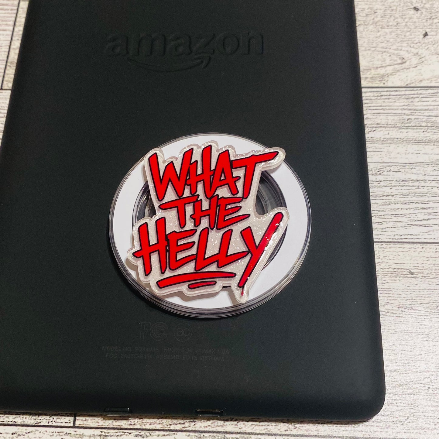 Round metal badge with red text 'WHAT THE HELLY' 