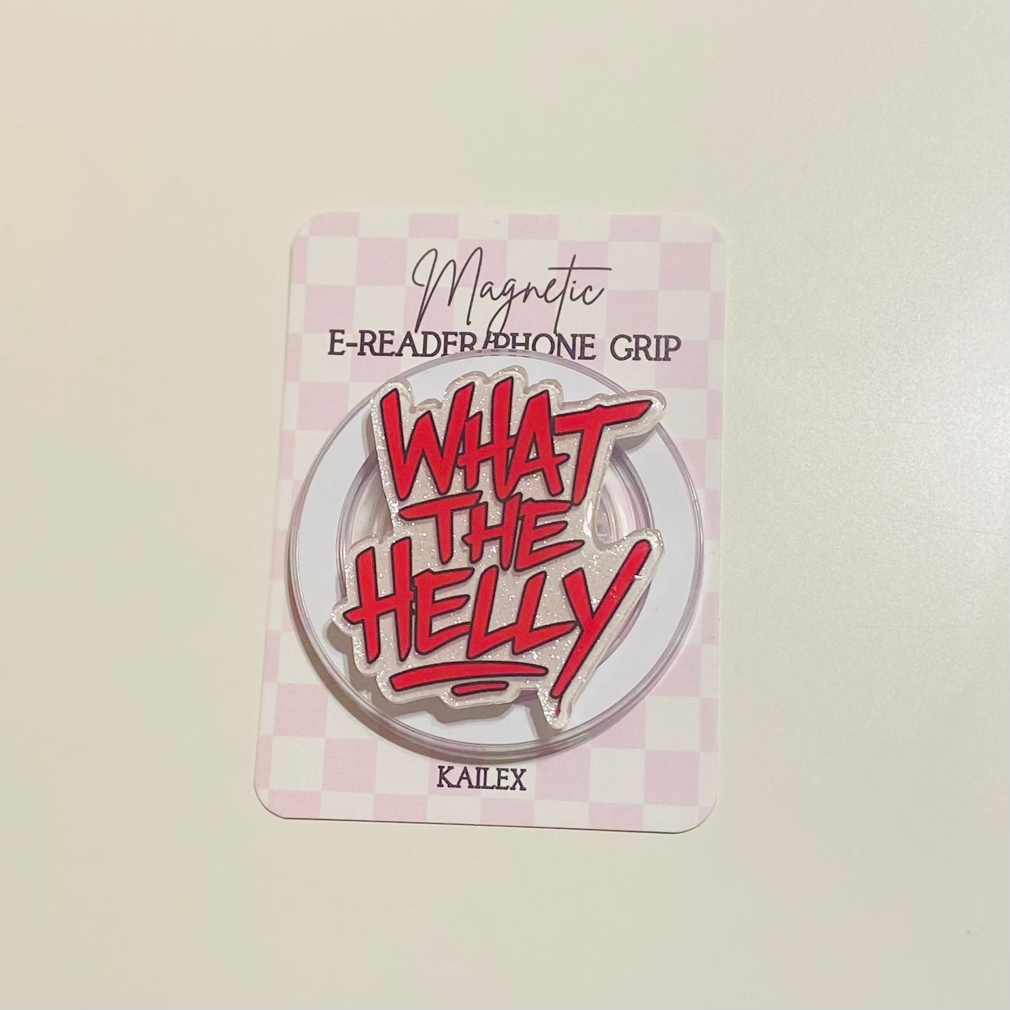 Round metal badge with red text 'WHAT THE HELLY' 