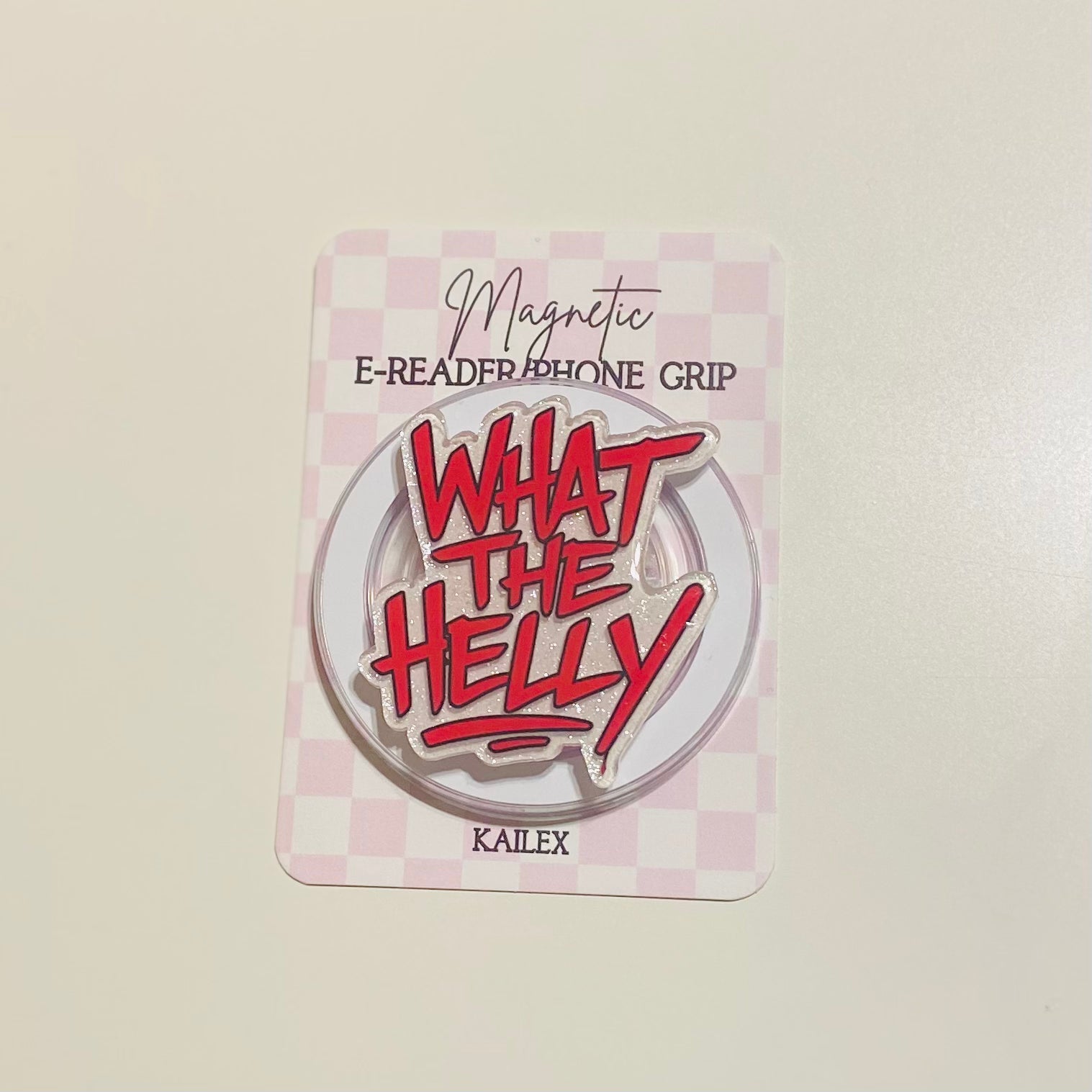 Round metal badge with red text 'WHAT THE HELLY' 