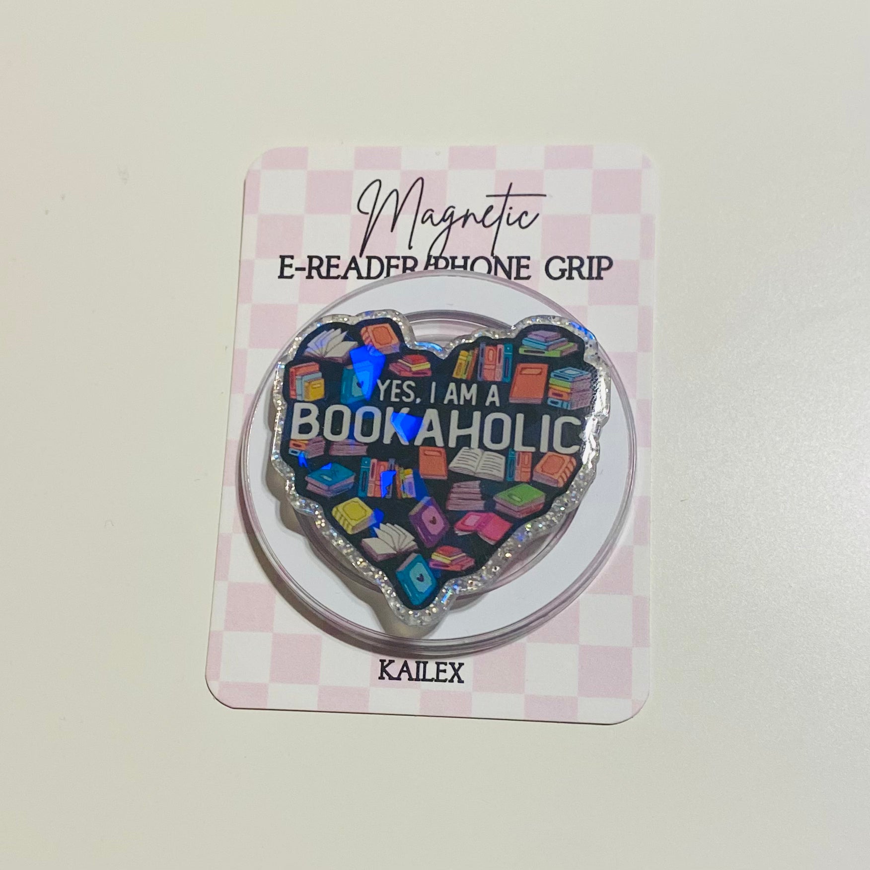Heart-shaped magnetic e-reader phone grip with 'Bookaholic' text on a checkered card, brand 'KAILEX' visible.