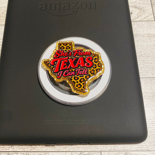 Decorative pin with 'She's From Texas I Can Tell' text on a black surface