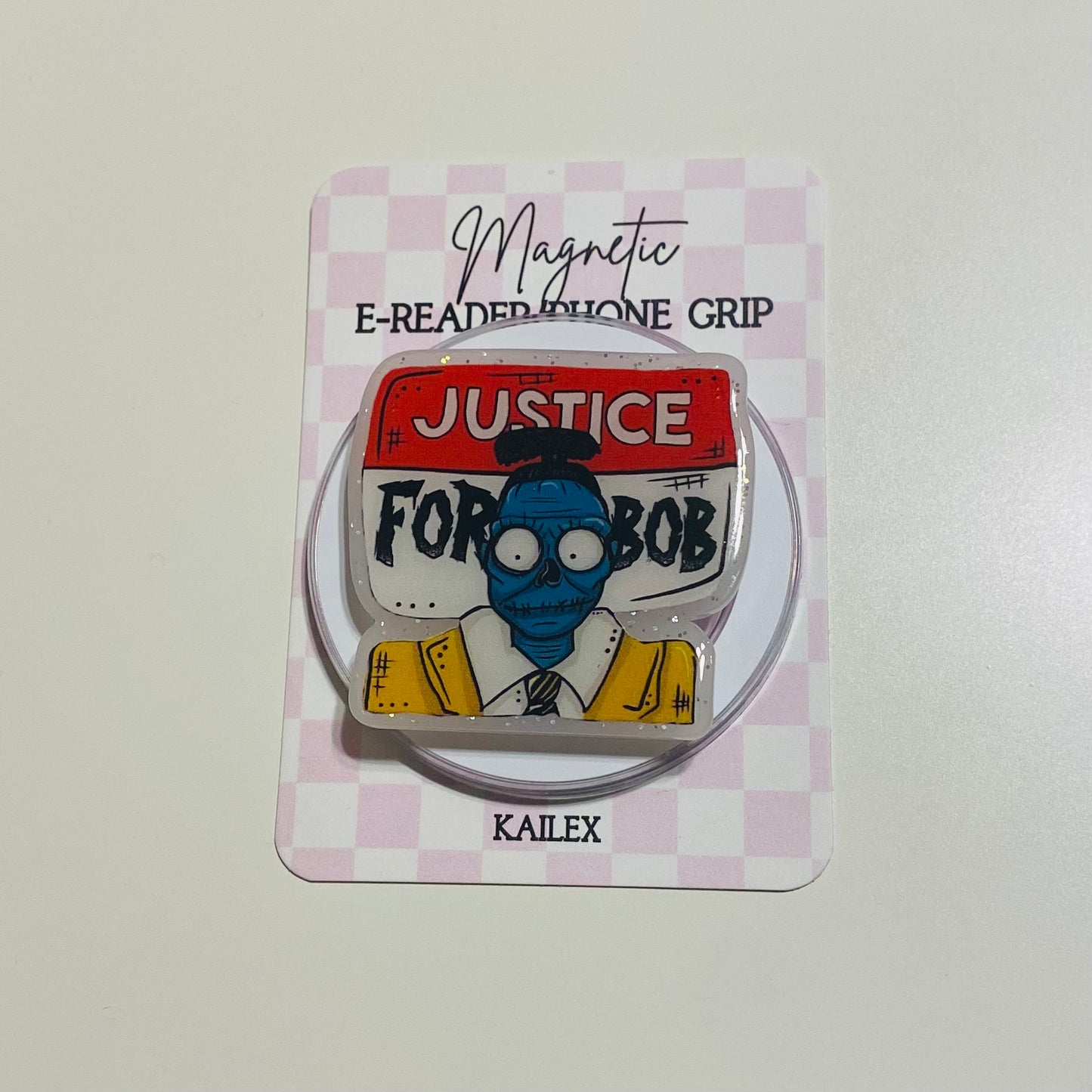Magnetic e-reader phone grip with 'Justice for Bob' design on a checkered background