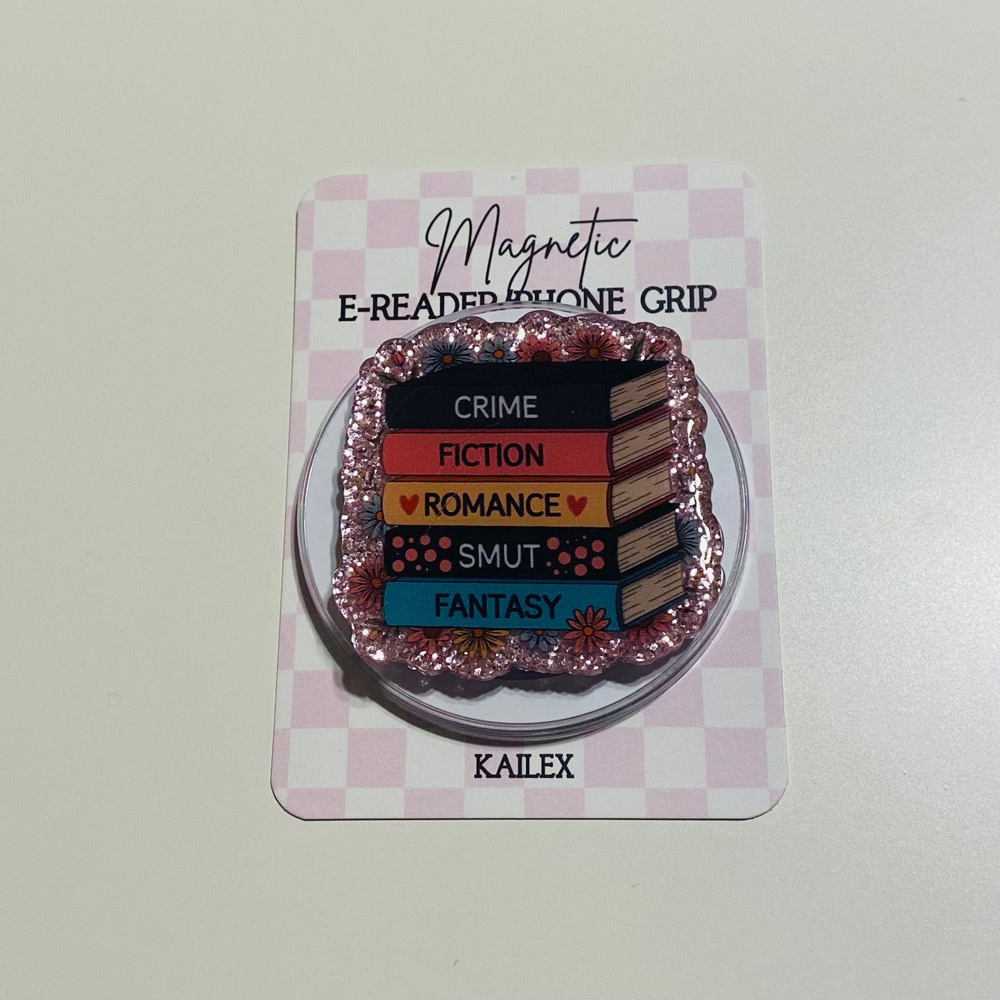 Magnetic e-reader phone grip with book genre text on a checkered card, brand 'KAILEX' visible