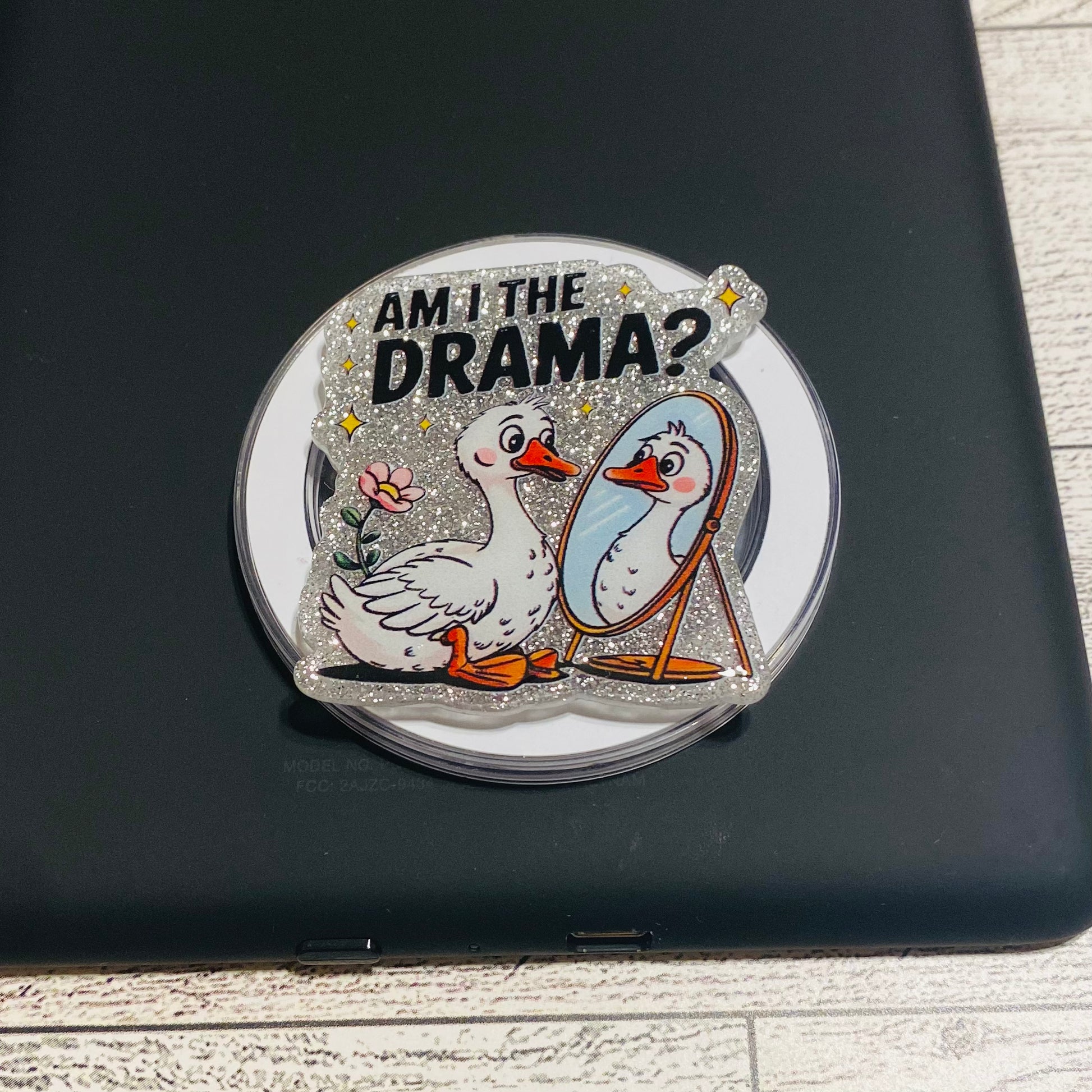 Decorative sticker with ducks and 'Am I the Drama?' text on a black surface.